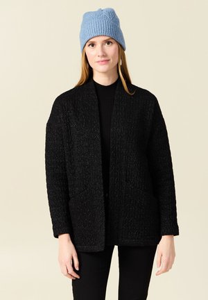 Schwarzer strukturierter Cardigan mit offenem Vorderteil und zwei Taschen, kombiniert mit einer hellblauen gestrickten Mütze, vor einem neutralen Hintergrund.