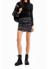 Svart långärmad topp med vita textmönster, matchad med en svart kjol med liknande text, samt svarta snörboots.