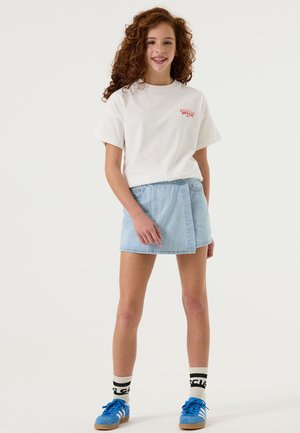 Camiseta blanca de manga corta con gráfico rojo, falda de mezclilla azul clara, zapatos deportivos azules y calcetas a rayas en blanco y negro.