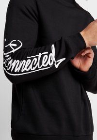 Felpa nera a maniche lunghe con lettering bianco che recita "Connected" lungo la manica sinistra. Realizzata in morbido tessuto texturizzato.