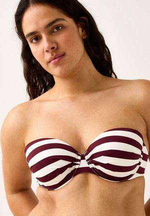 Donna con capelli lunghi e scuri che indossa un top bikini senza spalline a righe orizzontali color bordeaux e bianco su uno sfondo semplice.