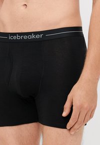 Boxer in cotone nero con vita flessibile e branding "icebreaker" in argento. Textura liscia, design aderente con tasca frontale.