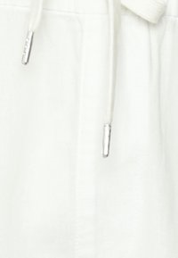 Białe lniane spodenki z wiązaniem w talii, zakończone srebrnymi metalowymi końcówkami na trokach i gładką fakturą.