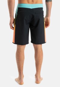 Bañadores negros con una cintura de color azul claro y paneles laterales en degradado de naranja a amarillo; fabricados con un material flexible y de secado rápido.