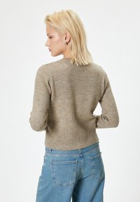 Maglione a coste beige con maniche lunghe, scollo rotondo e orlo aderente, abbinato a jeans a vita alta blu chiaro.