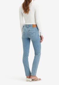 Svetle modré džíny s vysokým pasem a zúženými nohavicemi, denimová tkanina, zadní kapsy a hnědá kožená nášivka s logem na pase. V kombinaci s bílým topem.