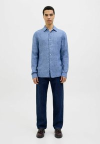 Camisa de lino azul claro con cuello abotonado, mangas largas y un diseño recto, combinada con unos jeans de pierna ancha azul oscuro y zapatos oscuros.