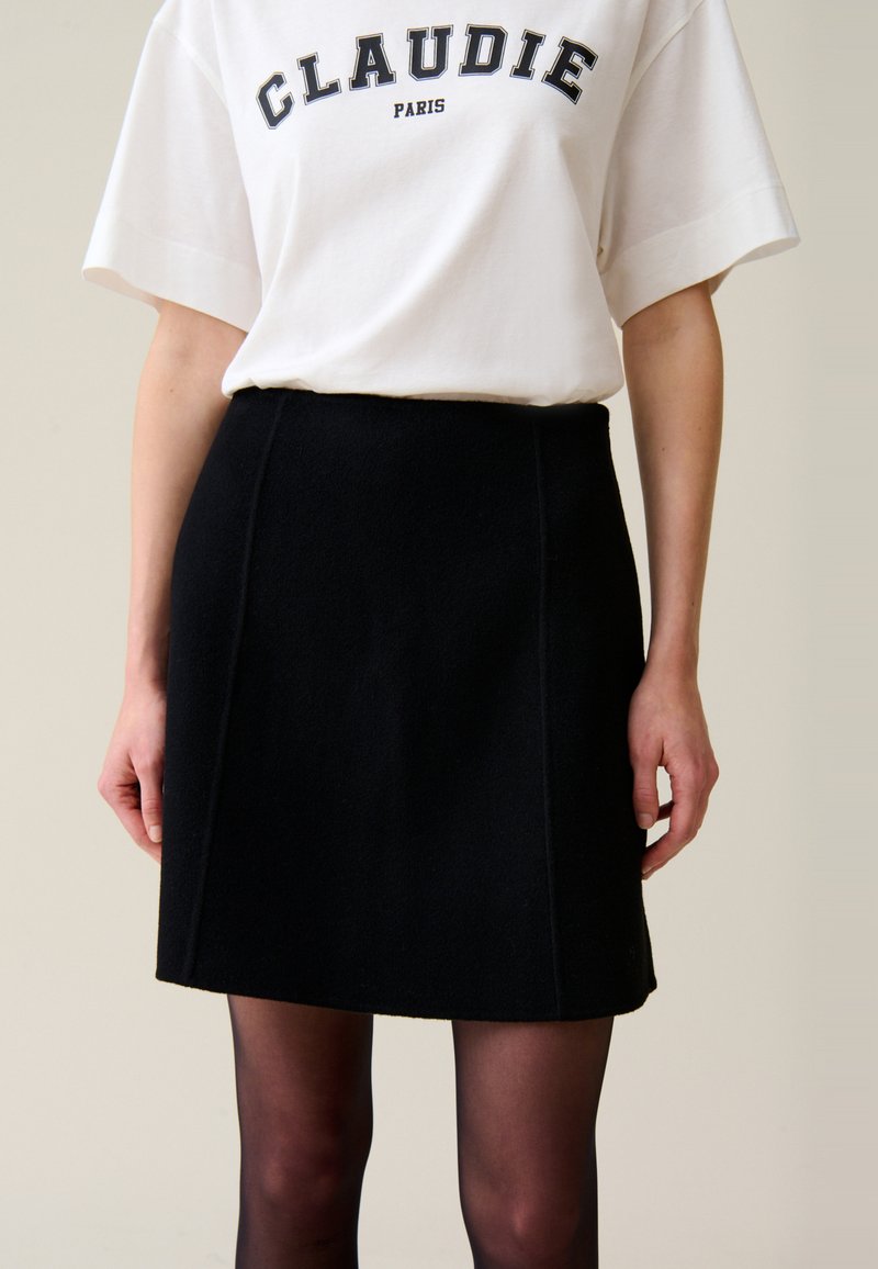 Falda mini de lana negra con una ligera forma de A. Textura suave y costuras laterales visibles. Combinada con una camiseta gráfica blanca.