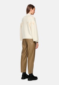Cream knitted oversized sweater with multicolored stitching, paired with brown faux leather trousers and chunky black ankle boots.