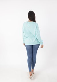 Maglione oversized azzurro chiaro con polsini e orlo a coste, abbinato a jeans blu attillati. Sfondo bianco semplice.