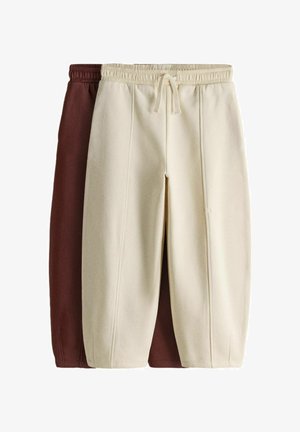 To par fleece-sweatpants, den ene i creme og den anden i brun, med elastiske taljebånd og forreste sømme, stablet med creme foran.