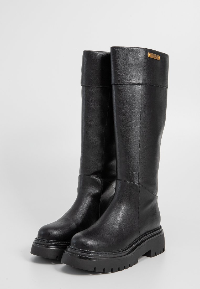 Schwarze kniehohe Stiefel aus glattem Leder, mit einer stabilen Sohle, breitem Schaft und einem dezenten metallischen Logo-Akzent an der Seite.