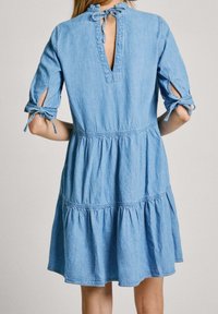 Světle modré džínsové šaty s vrstvenou sukní, tříčtvrtečními rukávy svázanými mašlemi a klíčovou vyříznutou zadní částí svázanou mašlí.