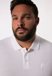 Biała koszulka polo wykonana z teksturowanej tkaniny z trzema guzikami. Posiada małe haftowane logo "M" na piersi.