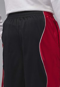 Μεσαίο τμήμα ατόμου που φοράει μαύρα και κόκκινα αθλητικά σορτς με λευκή επένδυση και ελαστική μέση, συνδυασμένα με λευκό μακρυμάνικο πουκάμισο.