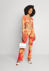 Conjunto colorido de duas peças que inclui um top cropped de manga longa com recortes e detalhes de laço, e calças largas com um ousado padrão gráfico em vermelho e amarelo.