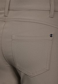 Helle braune Hosen mit einer glatten Textur, ausgestattet mit einer Gesäßtasche mit einem Knopfdetail und kontrastierenden Nähten entlang der Nähte.