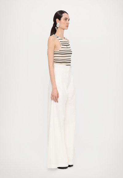 Top in tessuto a righe beige e nero, abbinato a pantaloni bianchi a vita alta e a gamba larga. Orecchini circolari di grandi dimensioni accentuano il look.