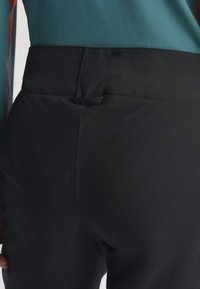 Čierne nohavice s hladkou textúrou, priliehajúcim strihom a diskrétnym detailom v podobe vrecka na zadnom páse.