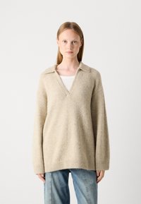 Beige strikket sweater med V-udskæring og krave. Lange, lidt oversized ærmer. Har en blød tekstur og ribbet kant.