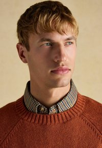 Oranž pleedigarderoob, millel on ribalaius, on kihtides kontrollitud särk, millel on rohelise, sinise ja beeži mustrid. Pehme tekstuur on nähtav.