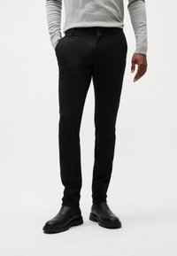 Pantalones de vestir negros con corte ajustado, hechos de una tela suave, con bolsillos laterales y un diseño limpio. Combinados con botas negras de tobillo.