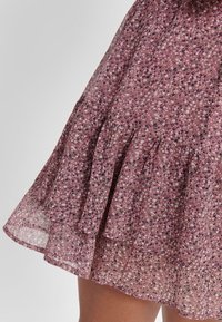 Jupe en chiffon rose à motif floral avec des volants et une texture légère et translucide. Conception de taille douce et froncée pour une silhouette fluide.