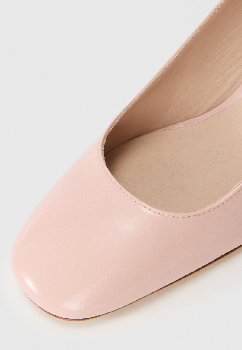 Różowe skórzane płaskie buty z zaokrąglonym kwadratowym czubkiem i gładkim wykończeniem. Wnętrze odsłania beżową podszewkę o subtelnej teksturze.