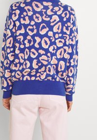 Pull bleu avec un imprimé léopard texturé en rose et blanc. Présente des poignets et un ourlet côtelés. Associé à un pantalon rose clair.