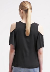 Sort koldskulder-bluse i blødt stof, med blonderelaterede detaljer ved skuldrene og afslappet pasform. Rund halsudskæring og korte ærmer.
