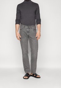 Grå polotröja, urblekta grå jeans och svarta sandaler. Jeansuren har rak skärning med subtila sömnadsdetaljer och fem fickor.