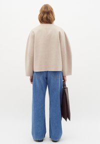 Šviesiai pilkas vilnonis kardiganas su per didelėmis rankovėmis, derinamas su šviesiai mėlynomis plačiomis kelnėmis. Laiko tamsiai rudu odiniu rankiniu maišu.