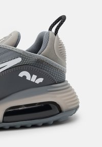 Šedá sportovní bota s prodyšným svrškem, s polstrovanou podrážkou a poutkem. Akcentováno bílým logem a texturovanými detaily paty.