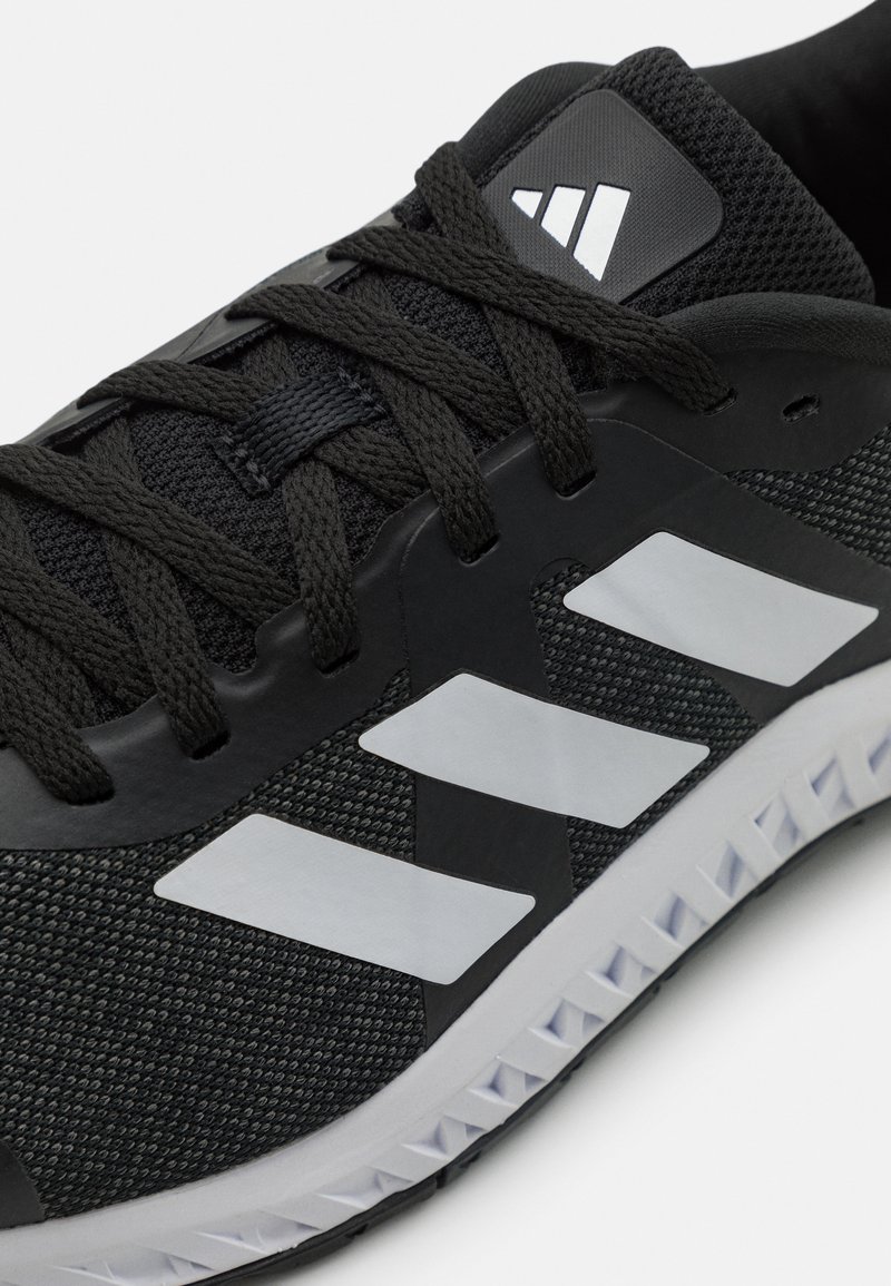 Czarne sportowe buty z siateczkowym wierzchem w odcieniu szarości, czarnymi akcentami i trzema białymi paskami. Posiadają teksturowaną podeszwę oraz wzmocnioną podpórkę pięty.