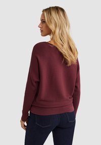 Bordeaux geribbelde trui met een relaxte pasvorm, lange mouwen en een brede halslijn, gecombineerd met donkere jeans in een casual look.