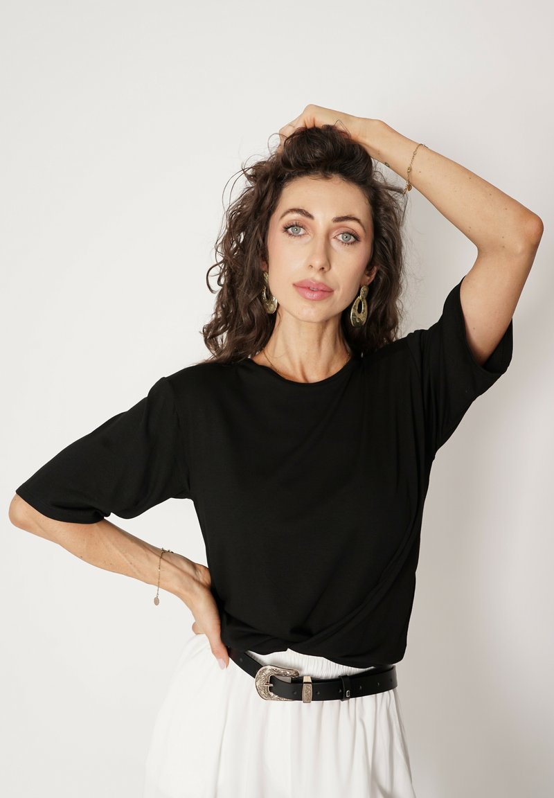 Czarny t-shirt z krótkim rękawem, lekki materiał, okrągły dekolt, noszony z białą spódnicą i czarnym paskiem z srebrną klamrą.