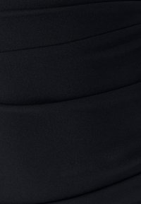 Tessuto nero con una texture liscia presenta morbide pieghe arricciate che creano una forma slanciata. Nessun motivo visibile o dettagli in metallo.