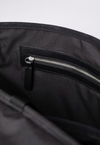Interno di una borsa nera in tessuto con una tasca con zip argento e un tirante nero, texture liscia e design minimalista.