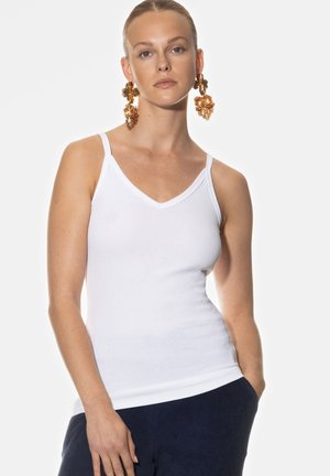Weißes, geripptes Tanktop mit dünnen Trägern und V-Ausschnitt. Das Modell trägt große, auffällige goldene Ohrringe. Hintergrund ist schlicht weiß.