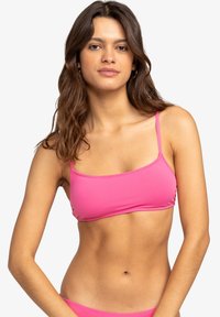 Top de bikini rosa con tirantes finos, con un diseño rectangular simple y textura de tela suave, usado por una modelo sobre un fondo neutro.