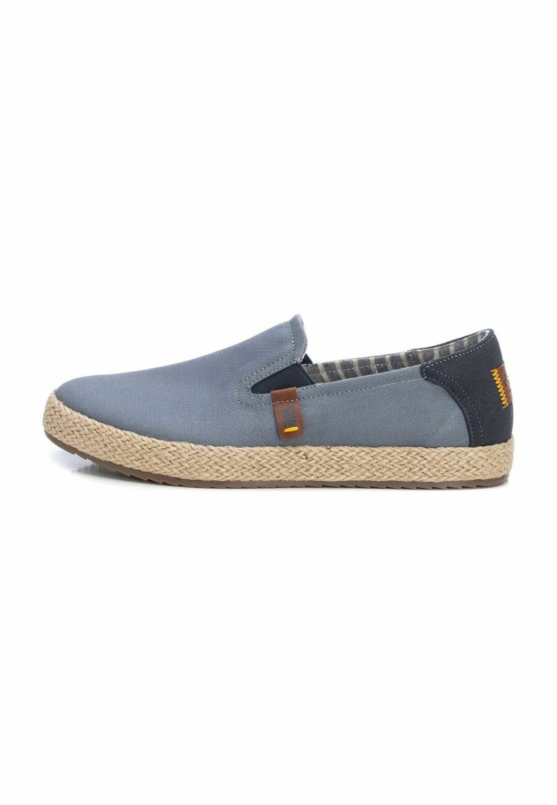 Zapato de los que se ponen fácilmente, en tela azul oscuro con suela de yute trenzada. Presenta detalles marrones y un forro a cuadros. Textura suave con forma redondeada.