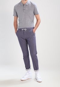 Šedá polokošile s krátkými rukávy a třemi knoflíky, spárovaná s tmavě modrými zúženými kalhotami s tkaničkovým pasem. Bílé tenisky, ohrnuté manžety.