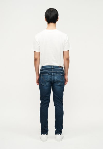 Mørkeblå denimjeans med slank pasform, synlige sømme på baglommen, kombineret med en simpel hvid t-shirt og hvide sneakers.
