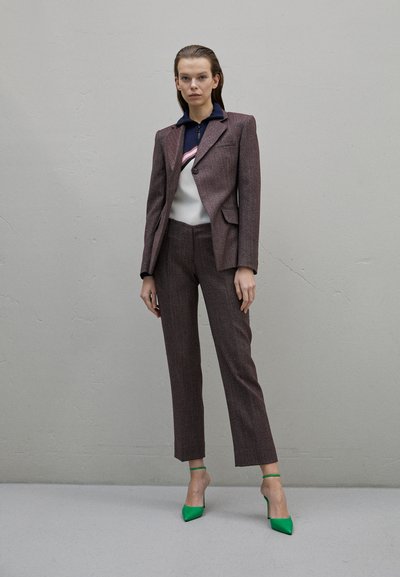 Καφέ υφασμάτινο κοστούμι με εφαρμοστό σακάκι και κοντό παντελόνι, συνδυασμένο με λευκή και ναυτική μπλούζα με ροζ ρίγα, και πράσινα ψηλοτάκουνα παπούτσια.