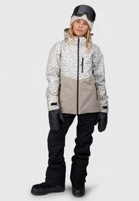 Jachetă izolată cu imprimeu leopard în bej și gri, asortată cu pantaloni de schi negri și mănuși, prevăzută cu fermoar frontal și buzunare cu fermoar.