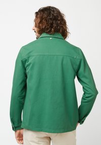 Groene katoen jas met een klassieke kraag, knoopmanchetten en een rugpand. Beschikt over een enkele metalen accent nabij de kraag.