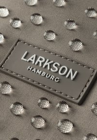 Borsa di tessuto grigia con accenti circolari in rilievo e superficie texturizzata. Etichetta "LARKSON HAMBURG" in gomma grigia, cucita sul materiale.