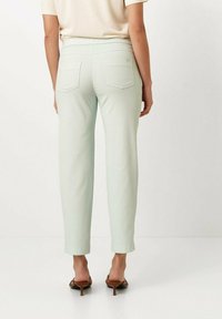 Lichtgroene, aansluitende broek van zachte stof, met een elastische tailleband en twee achterzakken, cropped boven de enkel, in combinatie met bruine hakken.