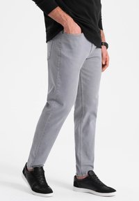 Šedé slim-fit džíny vyrobené z denimu, s klasickým pětikapsovým designem. V kombinaci s černými teniskami a černým tričkem s dlouhým rukávem.