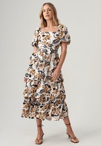 Floral maxi dress in white with black and gold flowers, square neckline, puff sleeves, tiered ruffles, and smooth fabric texture.